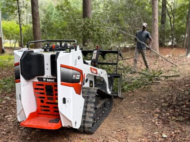 Bobcat excavator clearing branches in the woods