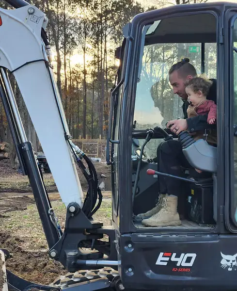 Man operating excavator with child passenger